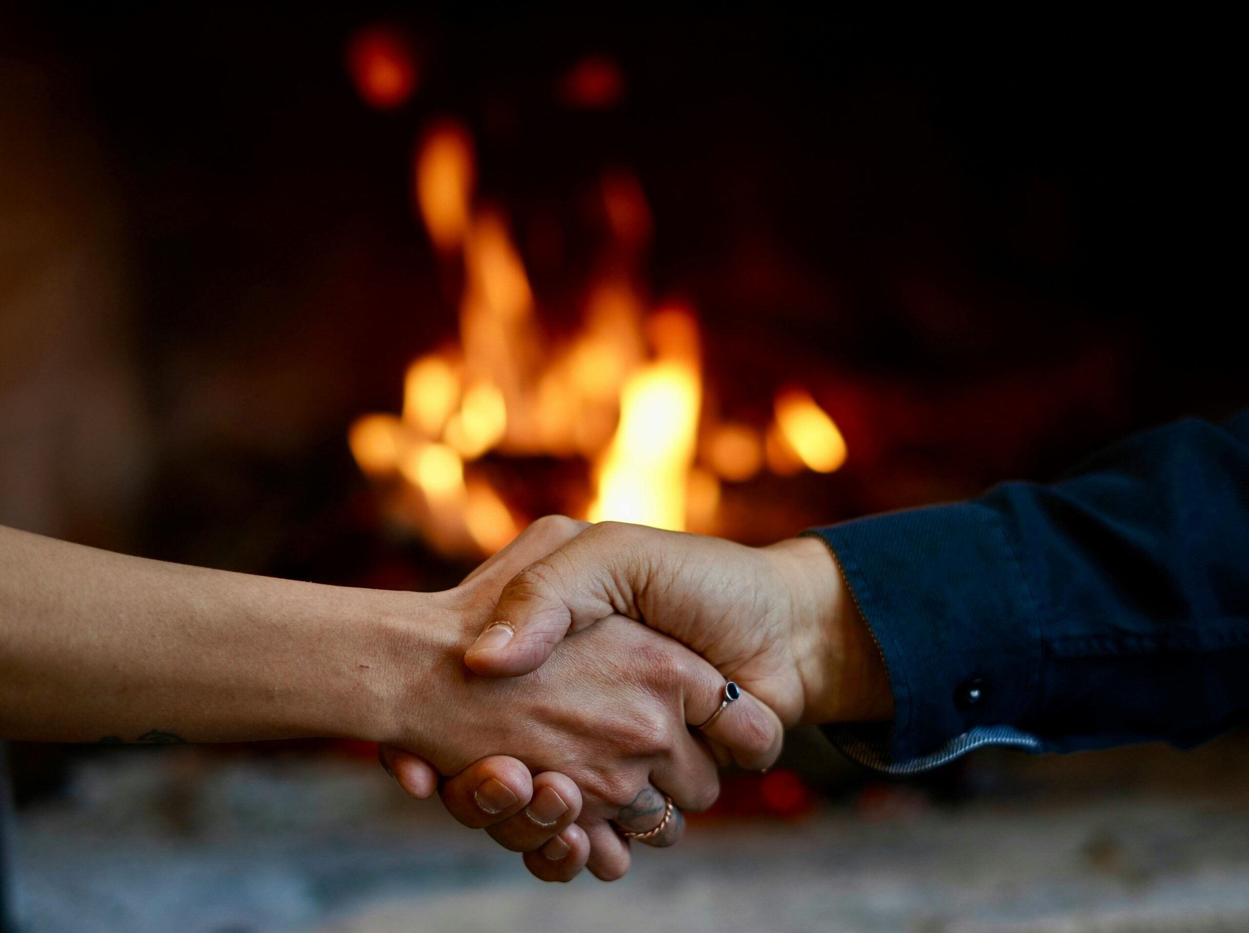Close-up of a handshake in front of a warm, glowing fireplace, symbolizing agreement and warmth.