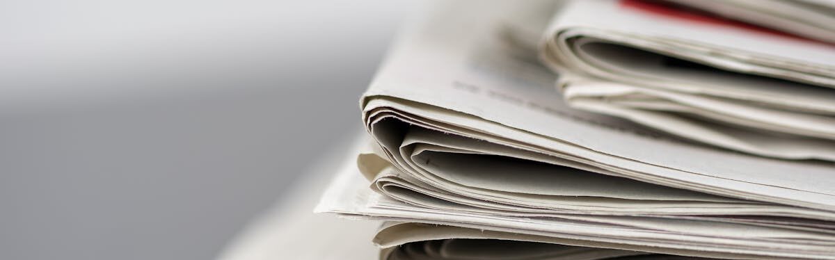 Close-up of stacked newspapers on a table, representing media and journalism.